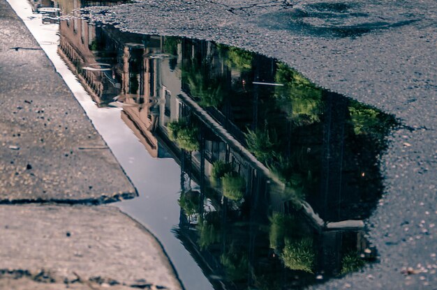 A close-up of a section of permeable pavement, showing water seeping through the porous surface into the soil below. The surrounding area is a residential street with houses and greenery.