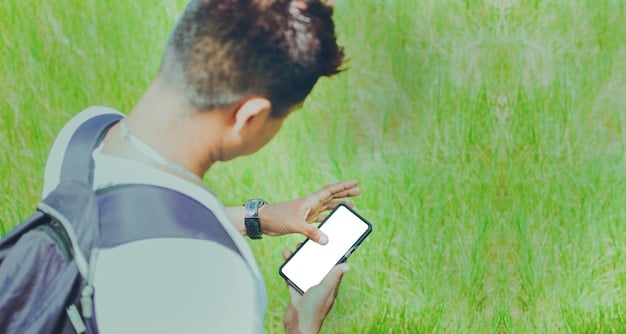 A person holding a smartphone with a citizen science app open, displaying a map interface for recording observations of plant species in a park. The person is wearing hiking boots and holding a field guide.